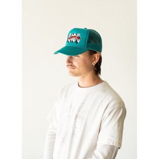 MODEL WEARING WELCOME SKATEBOARDS. JADE TRUCKER HAT WITH MESH BACK FOAM FRONT. SNAP CLASP. WELCOME LOGO WITH RED THORNS ACROSS LOGO ON FRONT. JADE BRAID ALONG BILL.