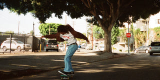 Skater pushing down a tree-lined street in light-blue pants and a brown jacket