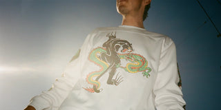 Skater in a white long-sleeve with a panther and dragon graphic, shot from below against the sky