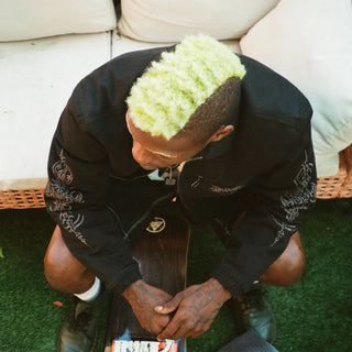 Overhead shot of a skater in a black embroidered jacket, sitting with a deck